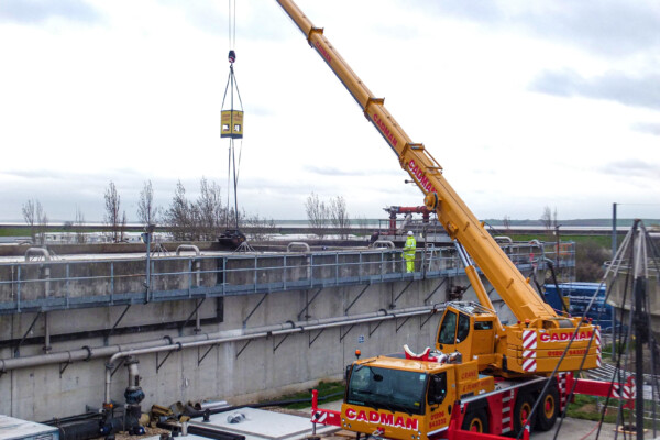 A mobile crane works at a wastewater facility with a remote-controlled grab