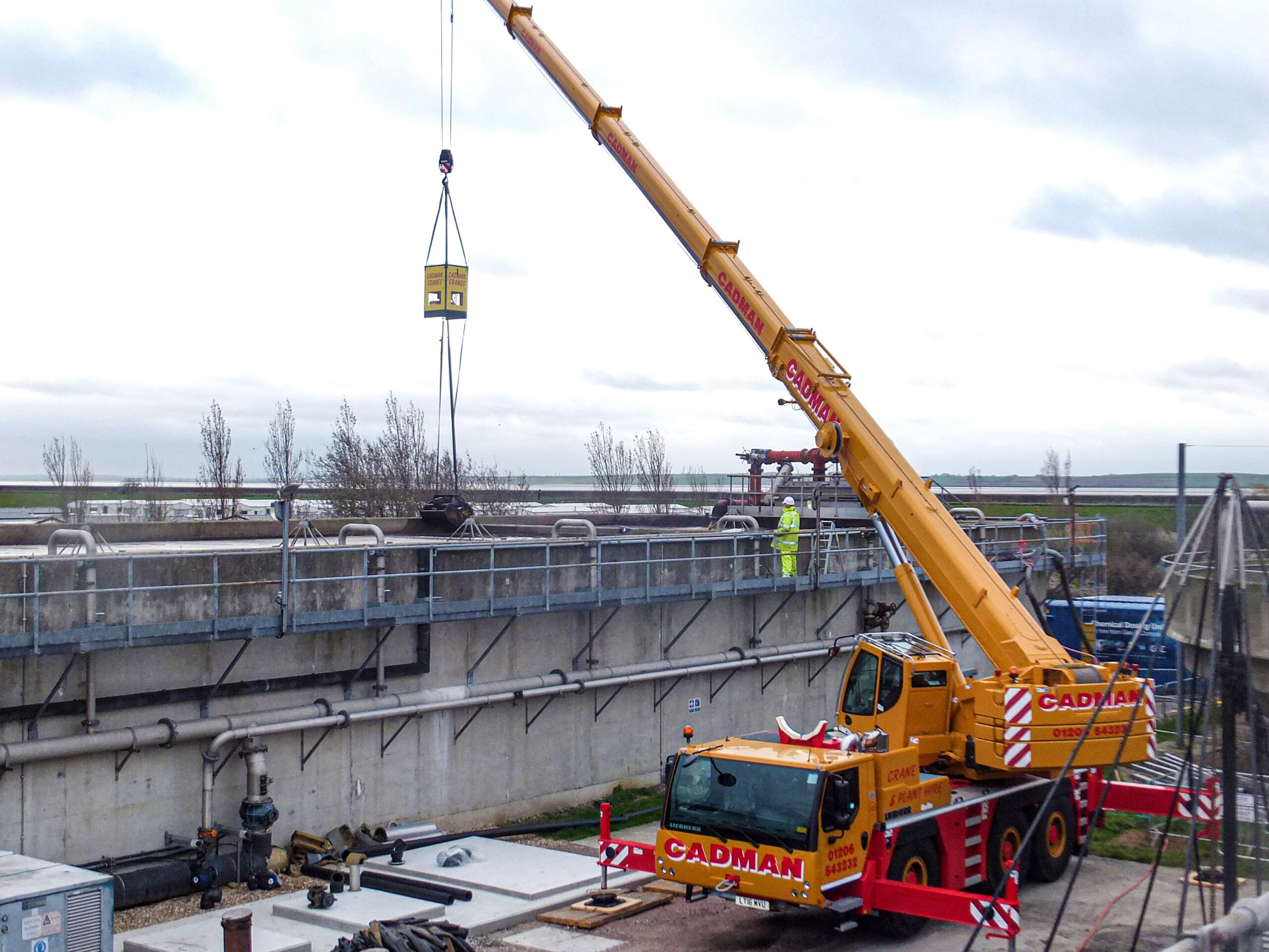 A mobile crane works at a wastewater facility with a remote-controlled grab