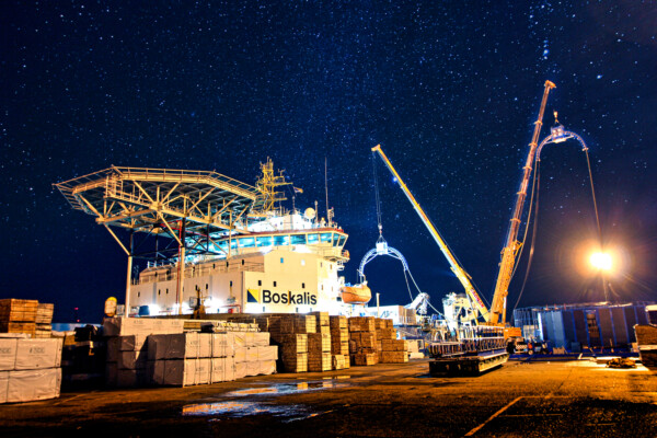 Two mobile cranes work at night in a port loading a ship with cabling