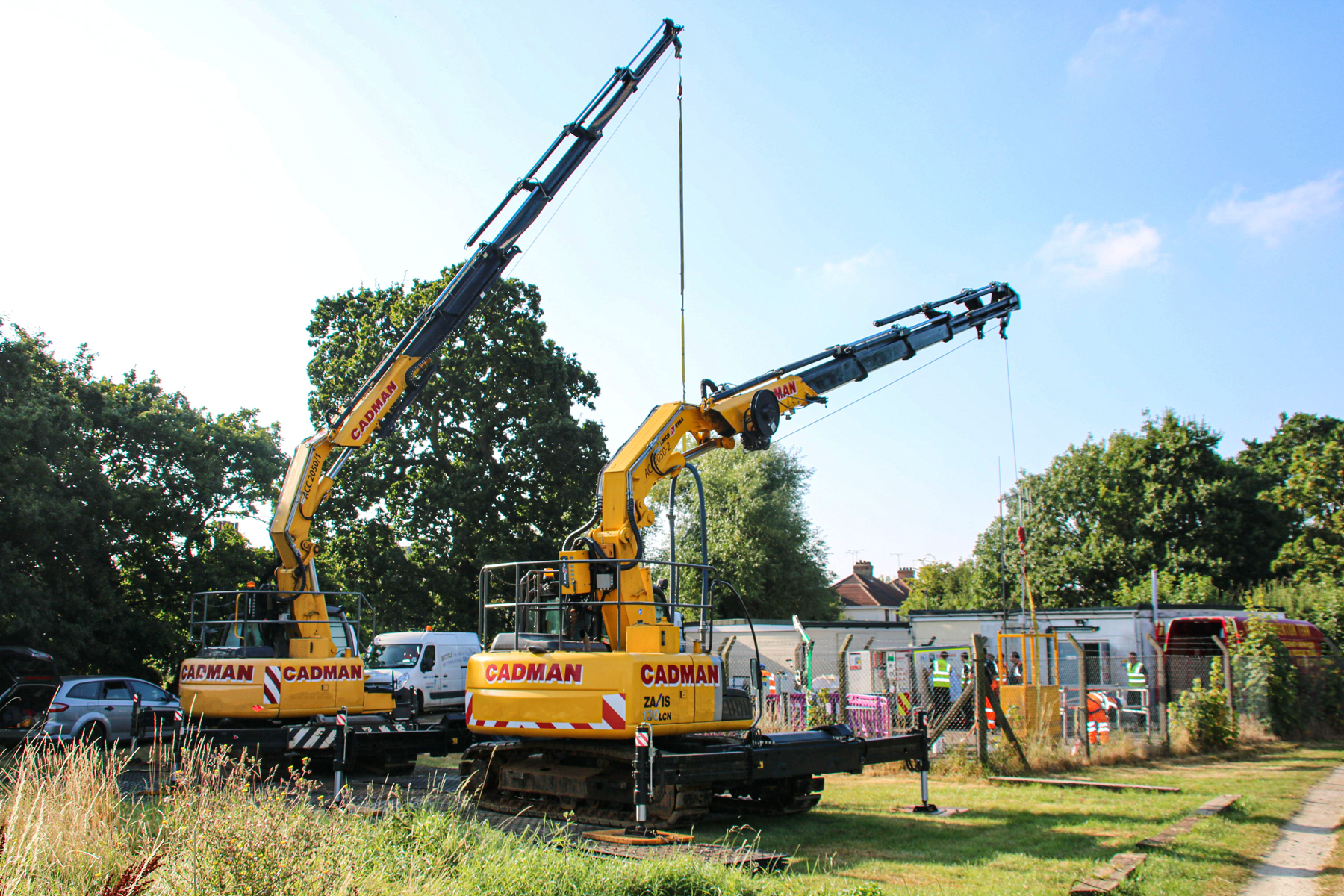 Two yellow compact crawler cranes sit next to each other working remotely in a field
