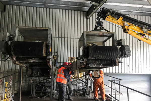 A compact crawler crane operates inside a commercial warehouse building to lift and install a piece of machinery