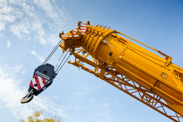 A yellow mobile crane boom is lifted up in the air with blue sky in the background