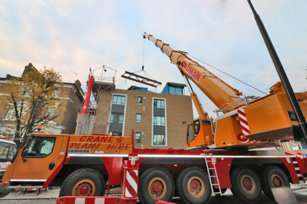 large mobile crane uses specialist lifting beams to install item onto residential roof