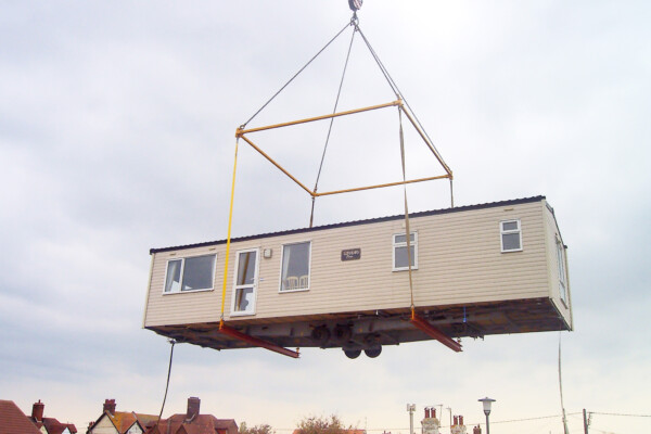 specialist lifting equipment on mobile crane holds static caravan in air during relocation