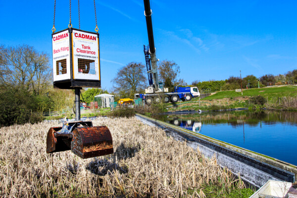 A large grab attachment on a mobile crane collects waste from a water treatment plant