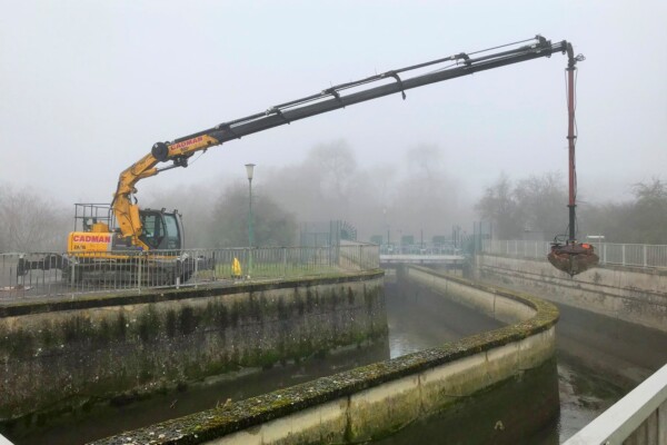 Compact crawler crane works in the fog to remove silt from a lake