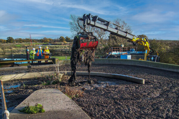 A compact mobile crane uses a grab to remove waste from a water tank