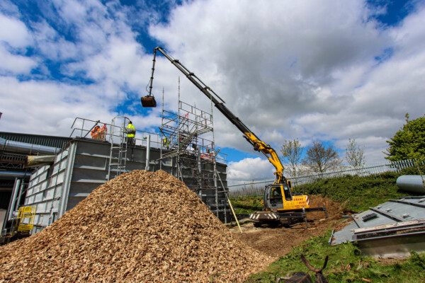 Compact crawler crane moves a pile of wood chippings into a biomass boiler with a grab attachment