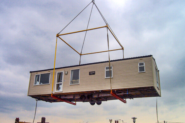 A caravan is suspended in the air using specialist lifting equipment attached to a mobile crane