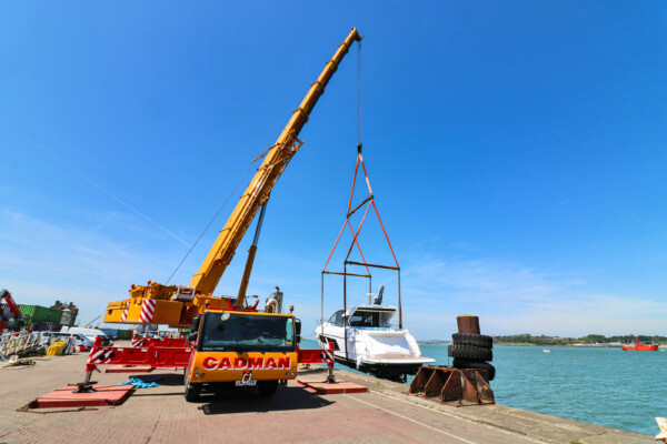 mobile crane suspends luxury boat over sea at port