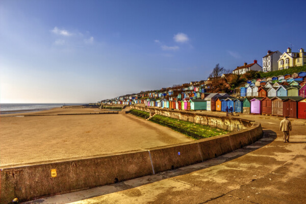 A wide angle photo of a beach in Essex with blue sky and a row of beach huts