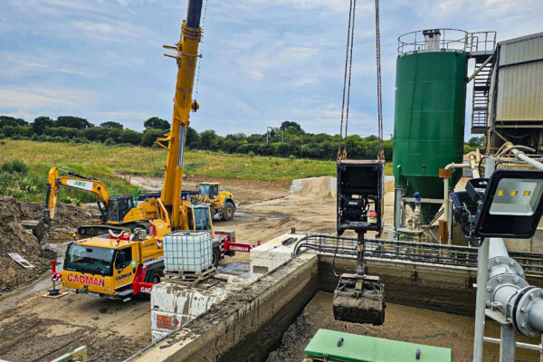 A yellow mobile crane works with a hydraulic grab attachment to move material