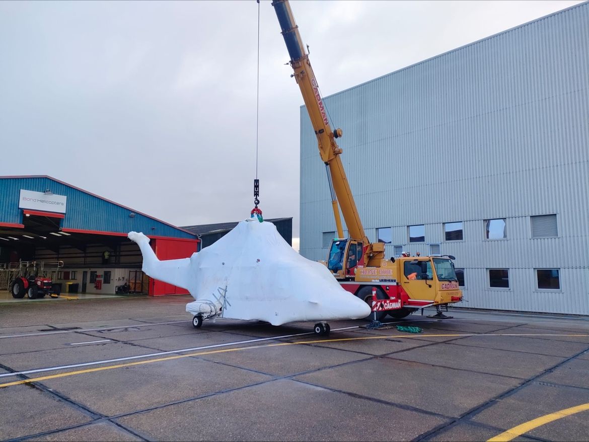 Helicopter wrapped in plastic lifted by mobile crane at Norwich Airport